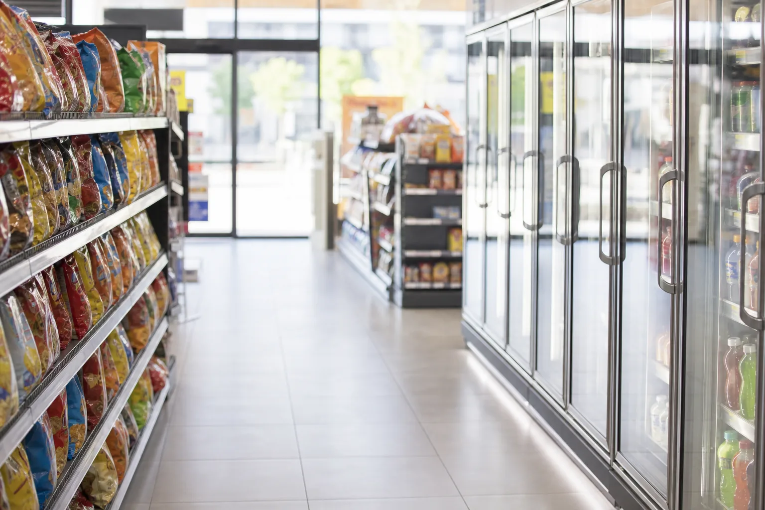 Neighborhood convenience store aisle with coolers and soft daylight near the entrance